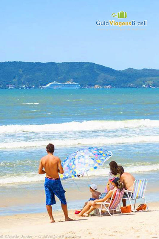 Imagem de uma família sentados com guarda sol na beira da praia.