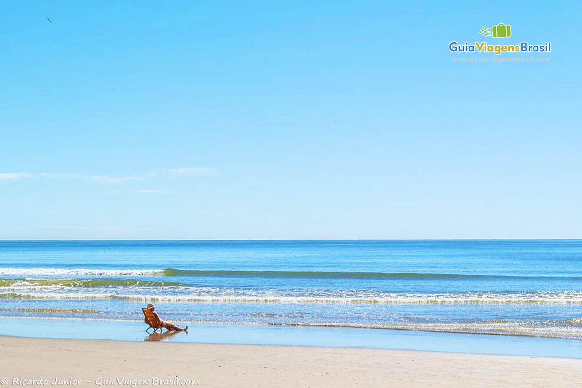 Imagem de uma pessoa sentada sozinha na beira da Meia Praia.