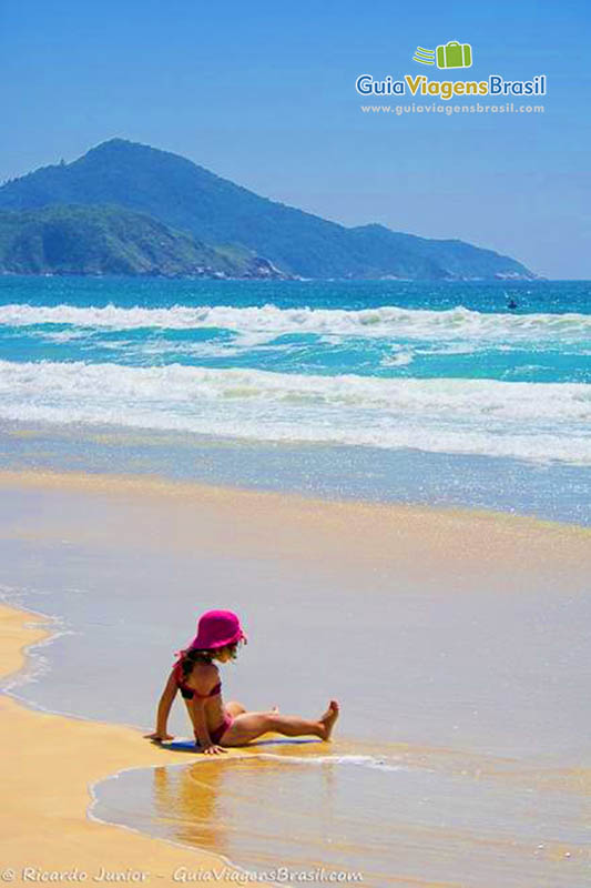 Imagem de menina sentada na beira da praia.