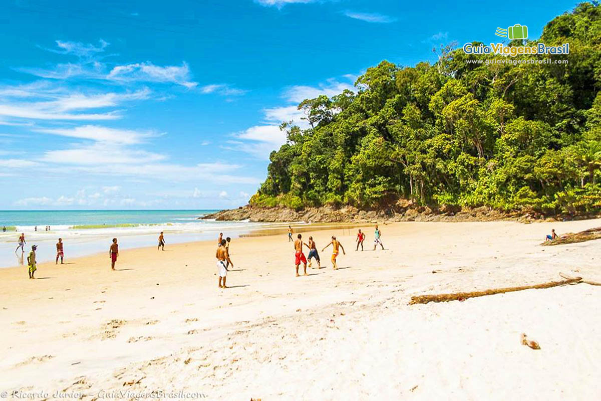 Imagem de rapazes jogando bola nas areias da linda praia.