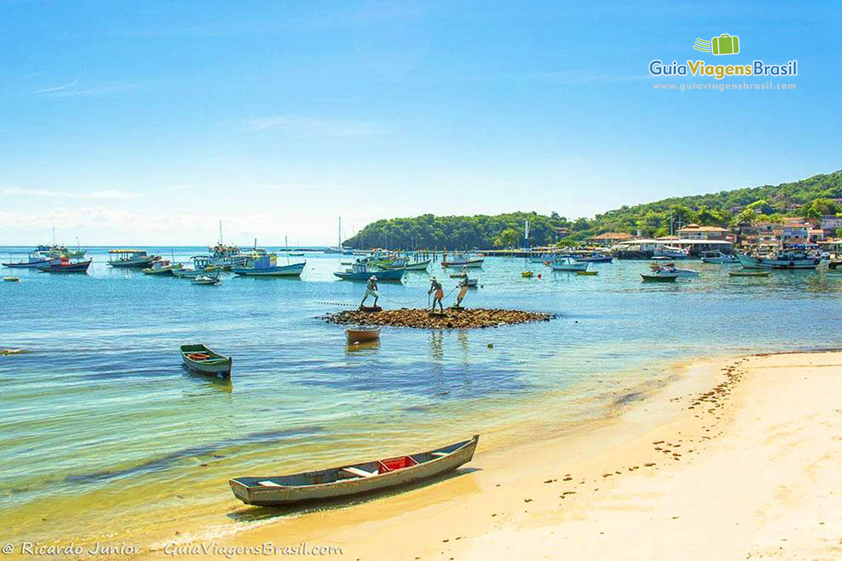 Imagem de barco na areia e do monumento dos pescadores ao fundo na beira da praia.