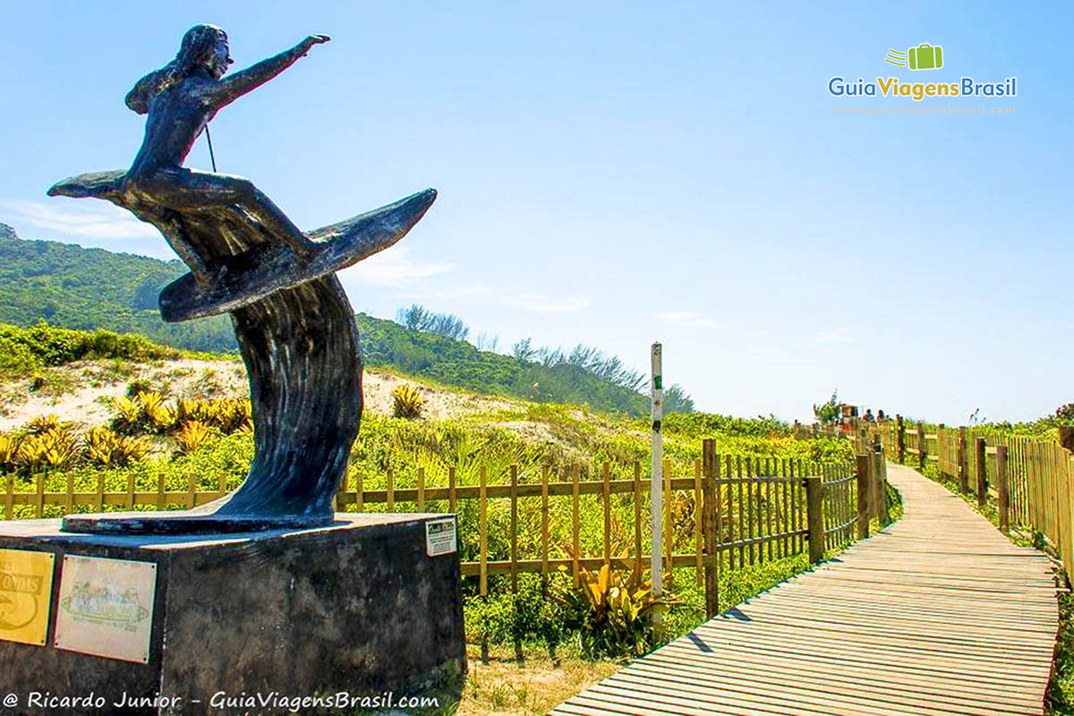 Imagem de um monumento que é um surfista na entrada da praia.