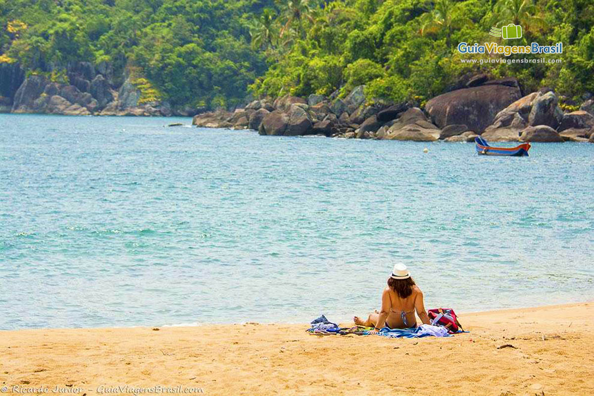 Imagem de uma mulher nas areias da praia tomando sol e curtindo a bela vista do mar.