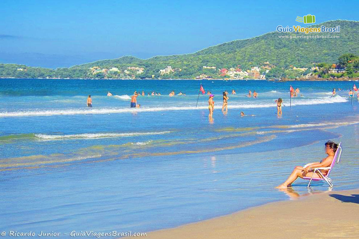 Imagem de uma moça sentada na cadeira de praia na beira do mar.