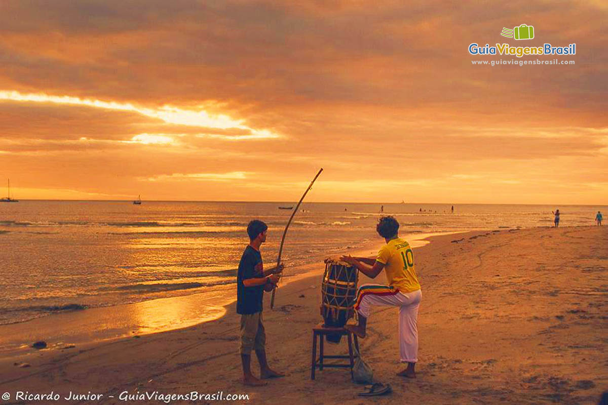 Imagem de dois rapazes fazendo som com berimbau e tambor para capoeira.