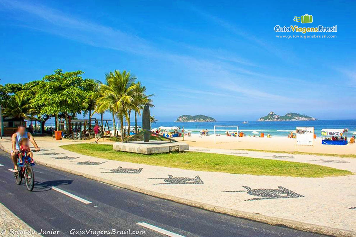 Imagem de uma moça andando de bicicleta na orla da praia.