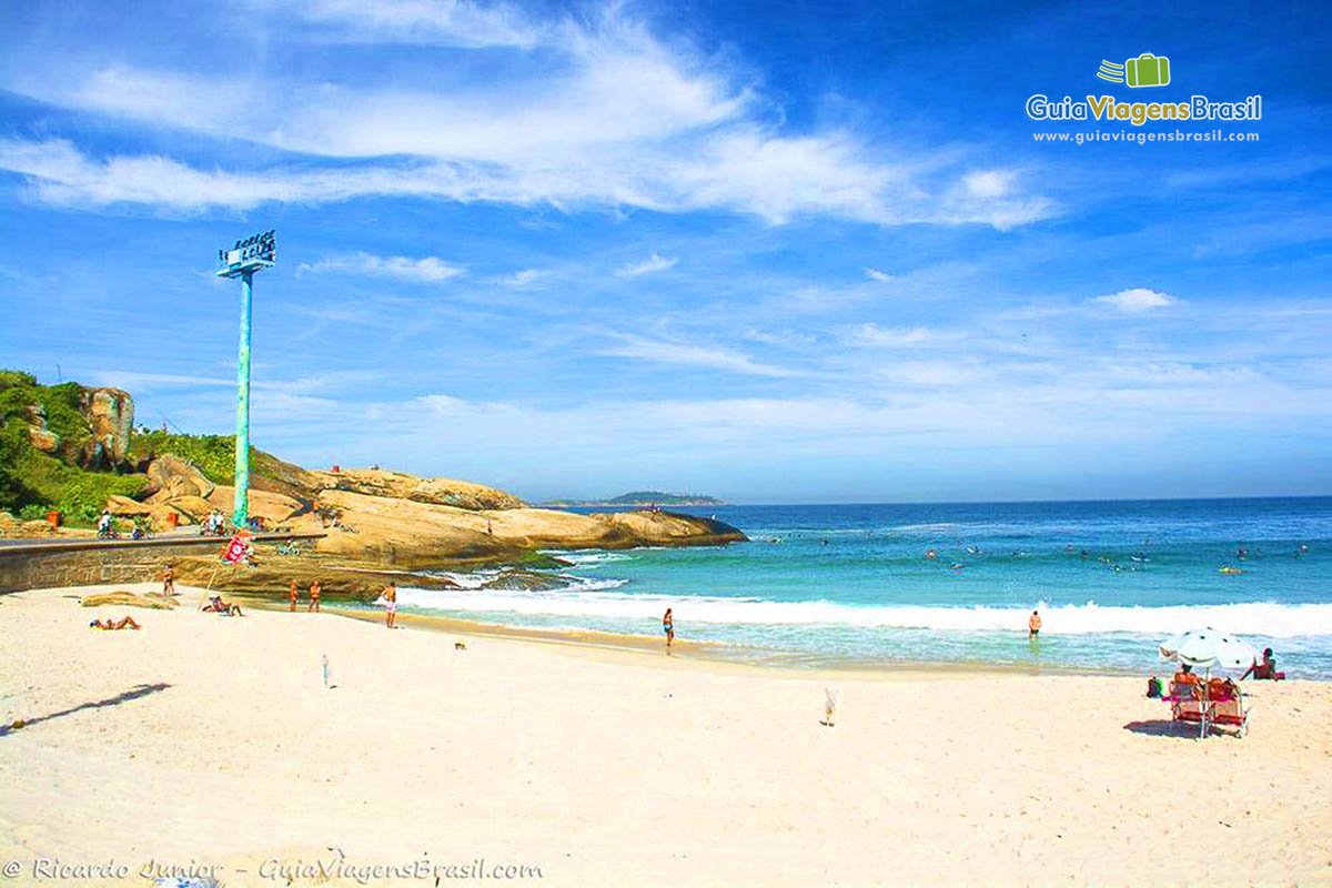 Imagem da praia e das pedras do Arpoador, onde as pessoas admiram o por do sol.