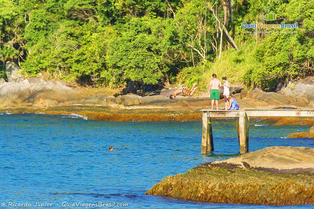 Imagem de adolescentes pulando das pedras para o mar maravilhoso.