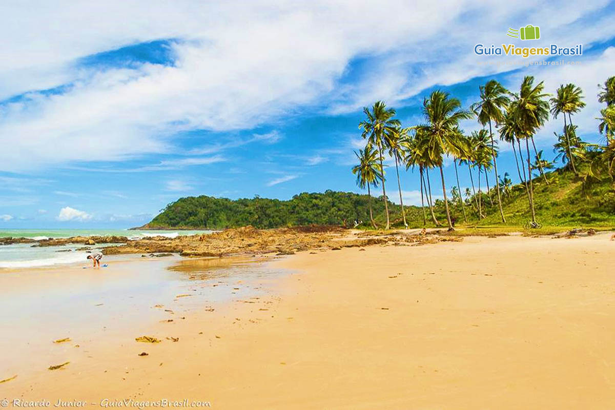 Imagem das águas claras e as pedras no canto da linda praia.