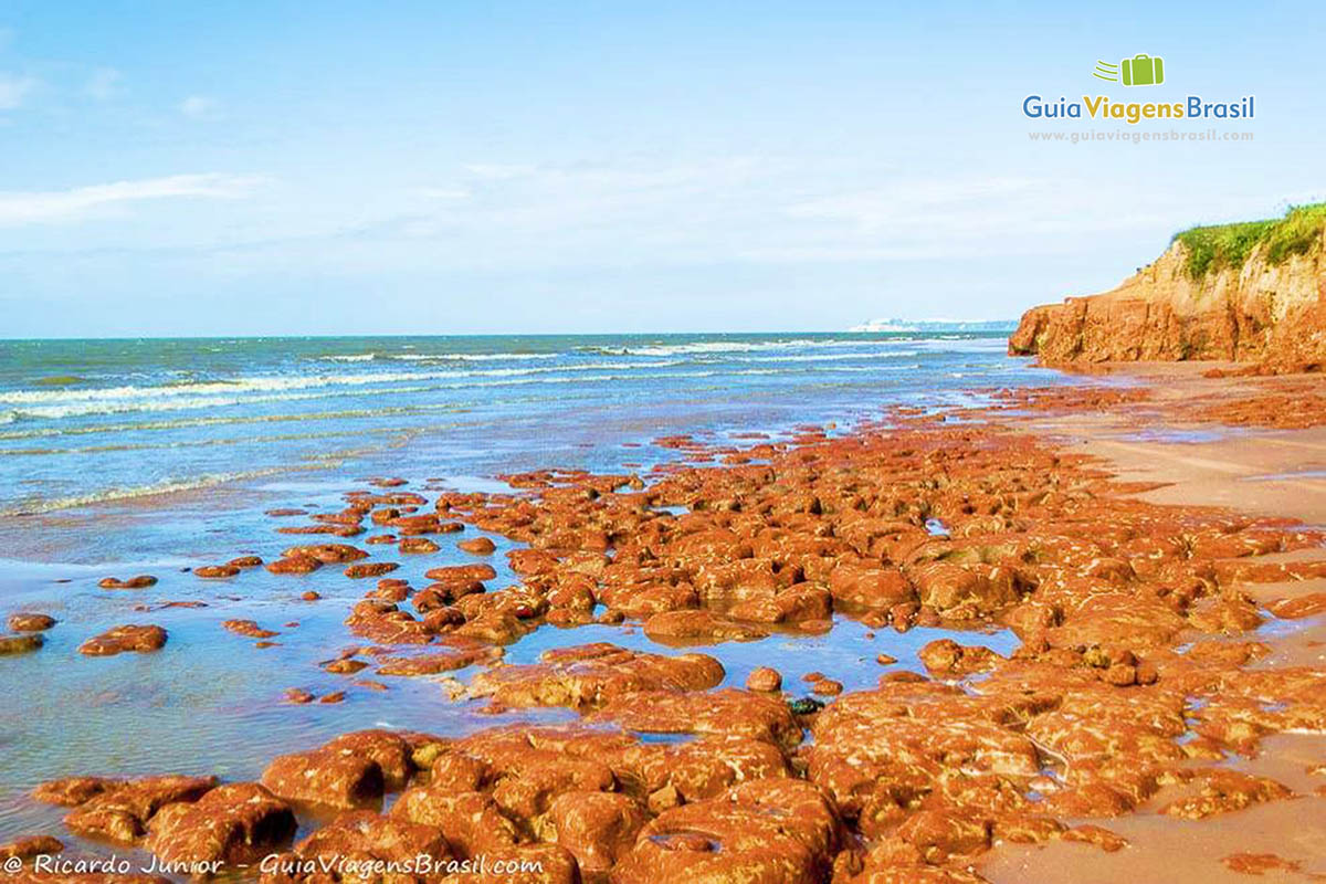 Imagem de umas pedras avermelhadas na beira do mar.