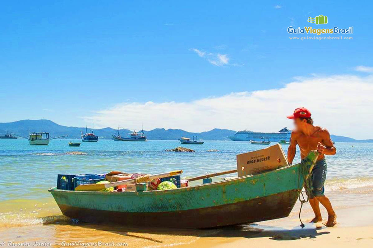 Imagem de pescador empurrando seu barco para o mar.