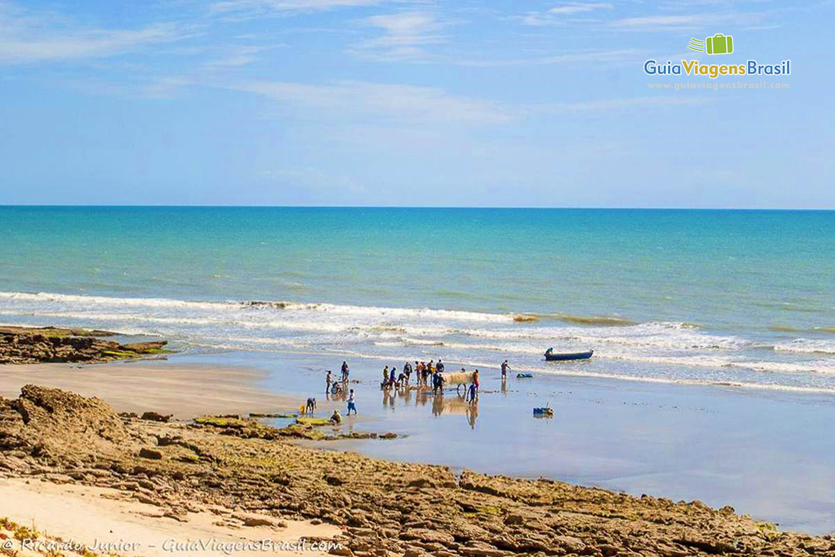 Imagem de pescadores na beira da praia carregando a rede.