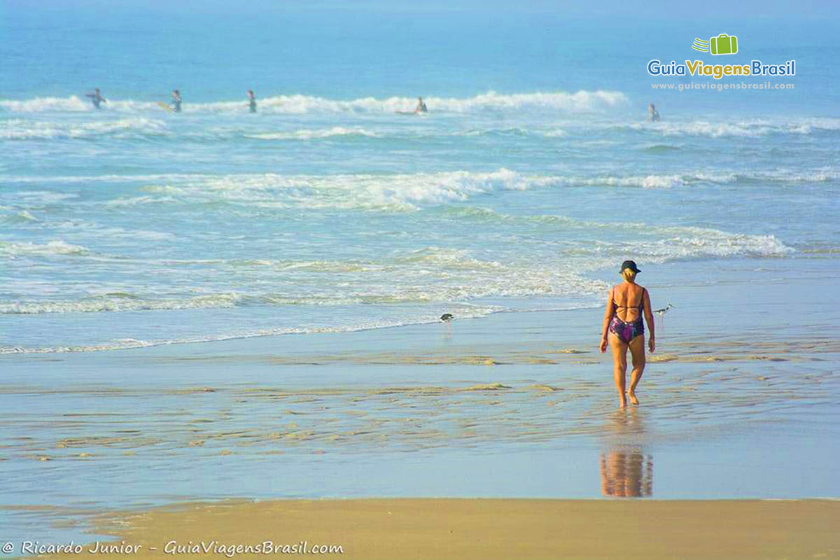 Imagem de uma pessoa admirando o mar e fazendo uma caminhada na beira da praia.