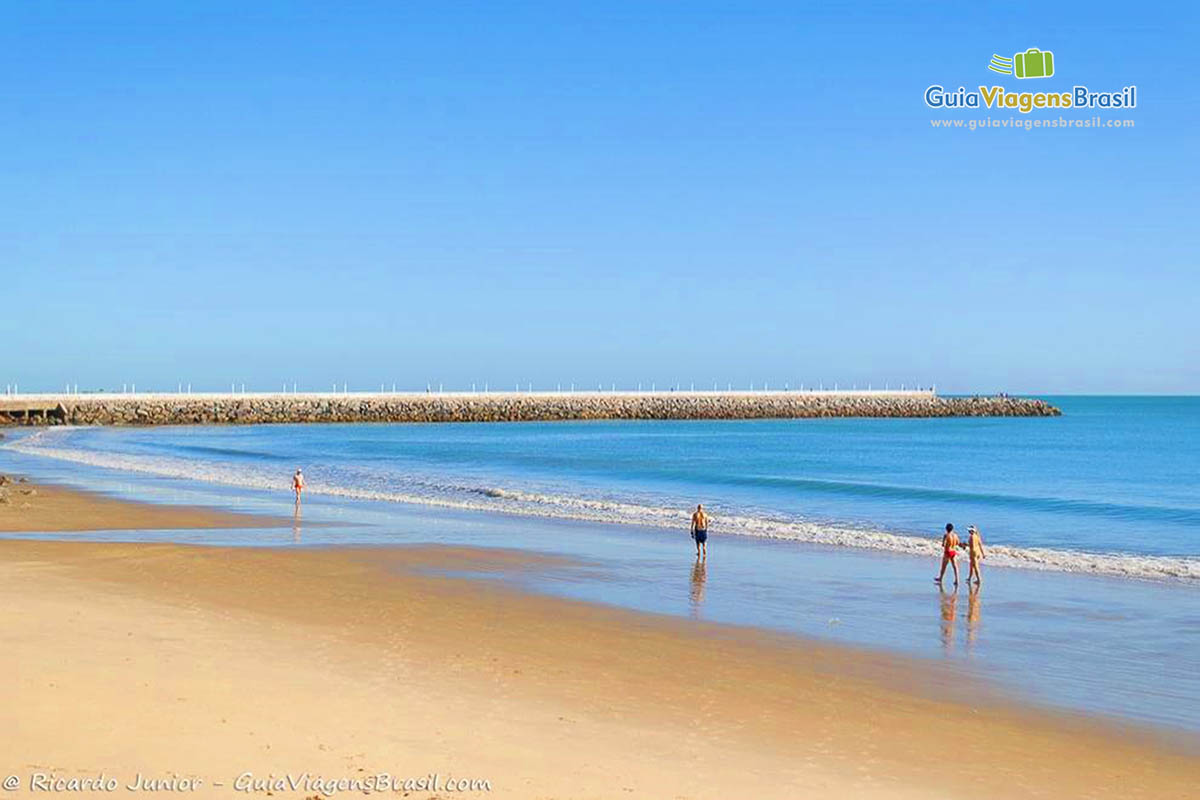 Imagem de pessoas caminhando e ao fundo caminho para mirante com mar azul encantador.