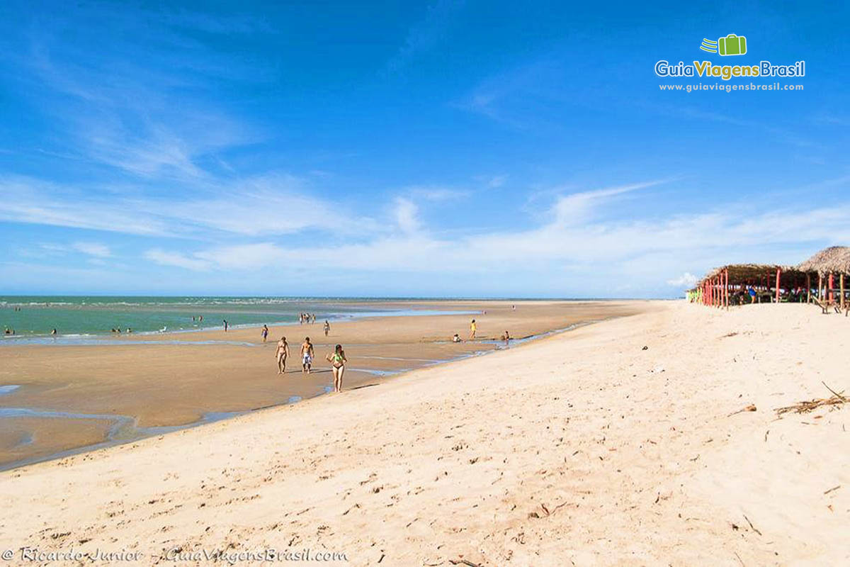 Imagem de pessoas andando pela grande faixa de areia.