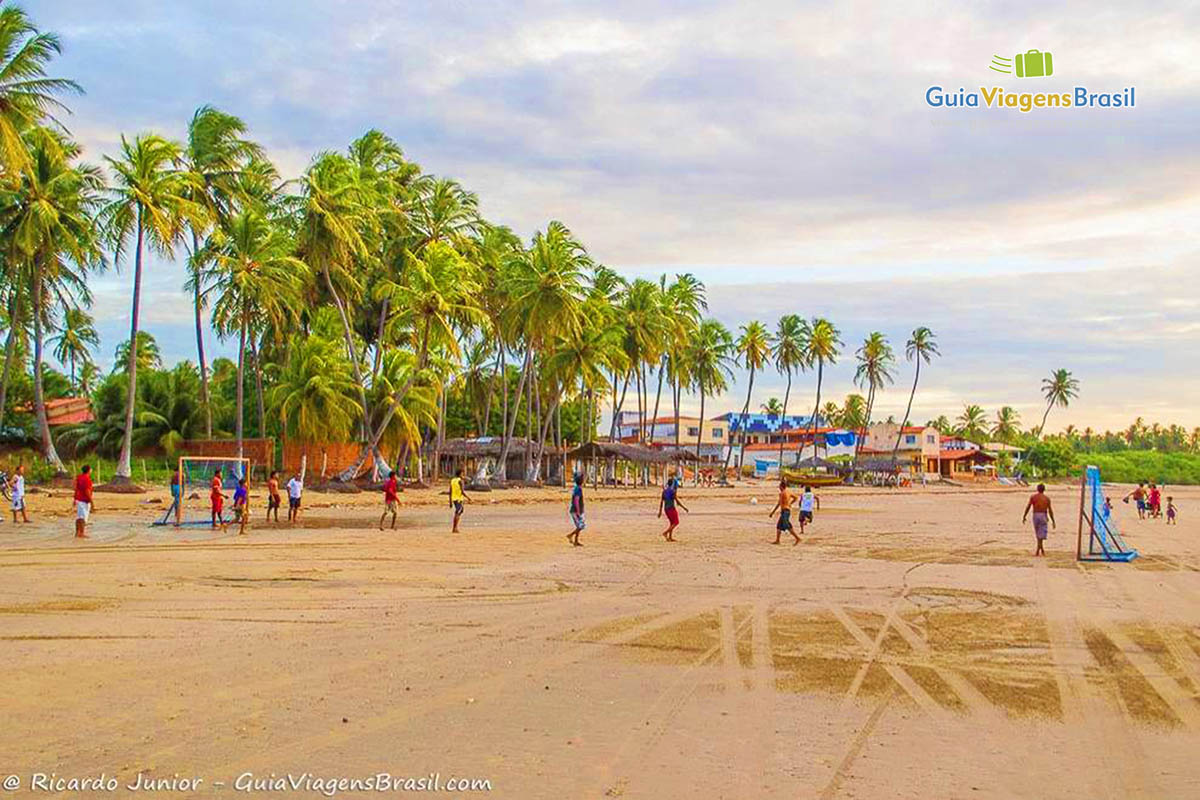 Imagem de lindos coqueiros na orla da praia e rapazes jogando bola.