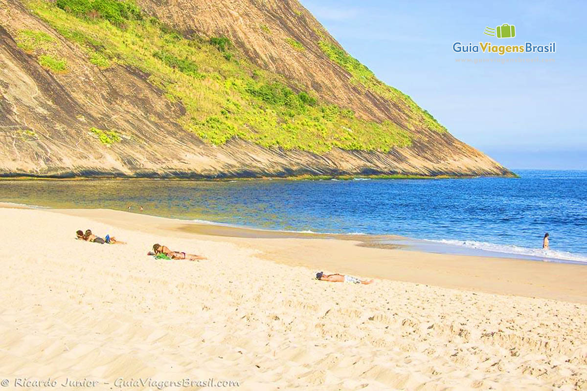 Imagem de pessoas deitadas na areia da praia curtindo um belo dia de sol.