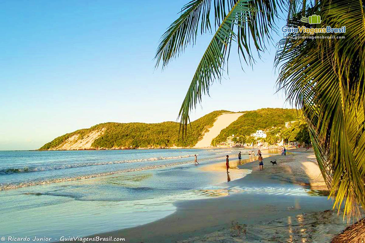 Imagem de lindo entardecer com turistas na Praia Ponta Negra.