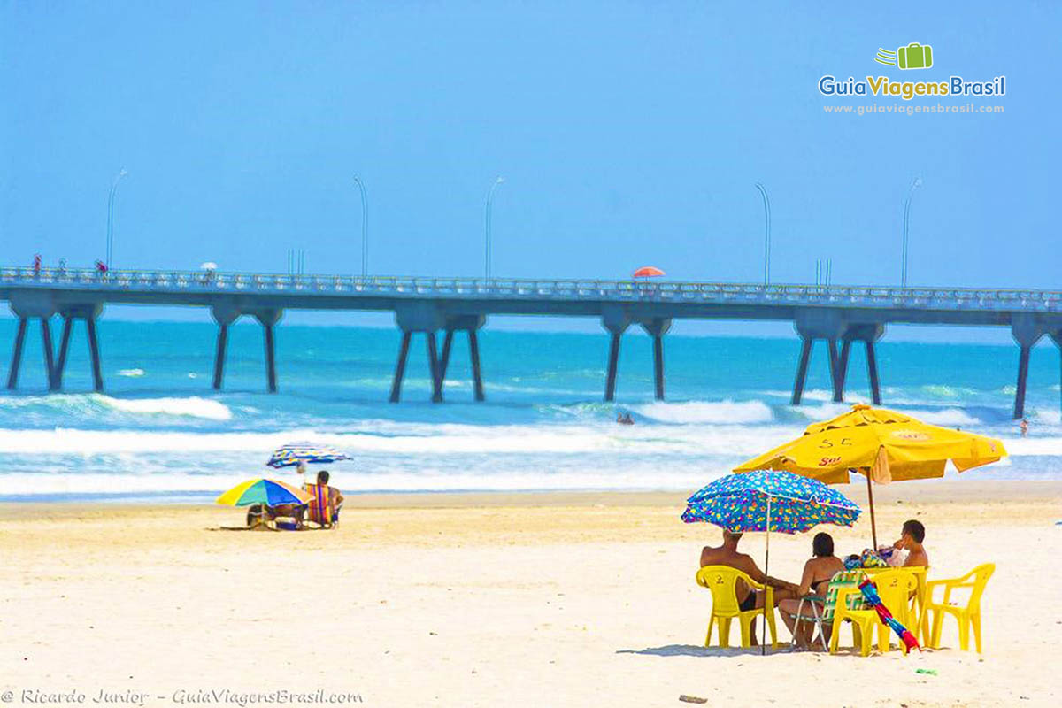 Imagem de turistas na praia e ao fundo a ponte de Mongaguá.