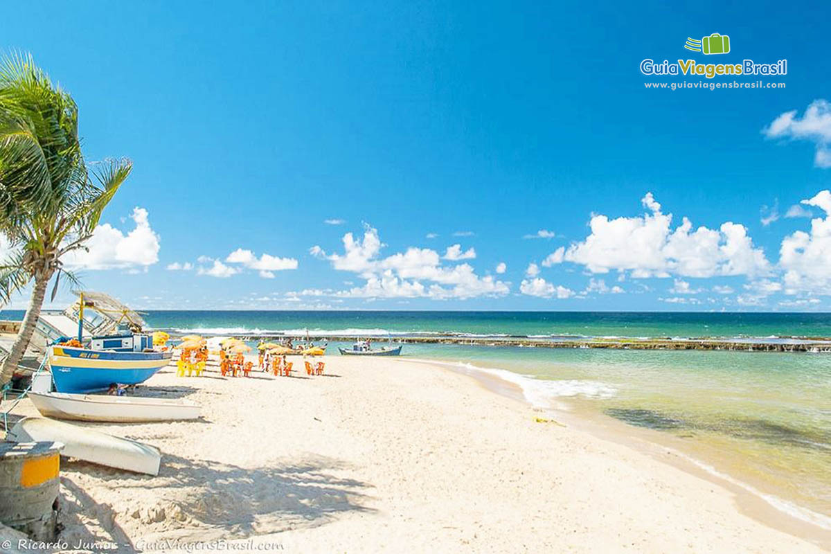 Imagem de cadeiras nas areias e ao fundo recifes no mar.