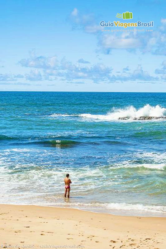 Imagem de um turistas em pé na beira da praia admirando as belezas naturais.
