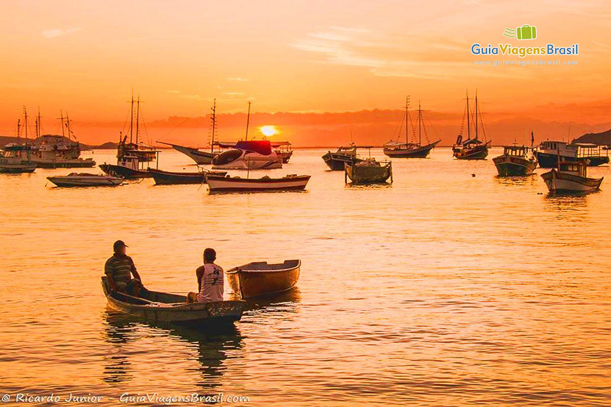 Imagem de pescadores sentados em seu barco admirando o por do sol.
