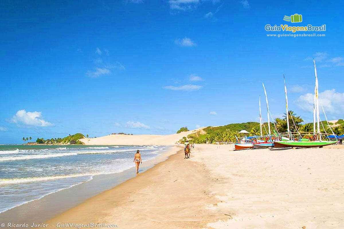 Imagem de uma turistas andando na beira da Praia de Genipabu.