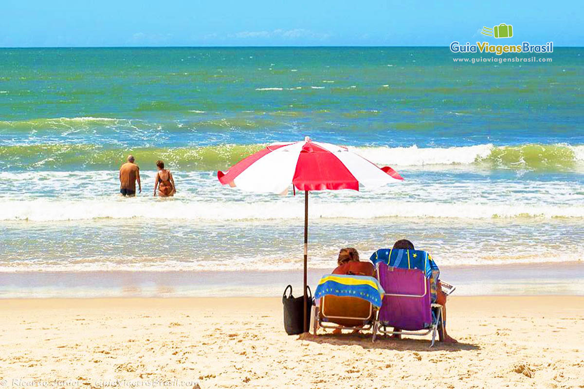 Imagem de casal na areia e outro casal nas águas da Praia Itapema.