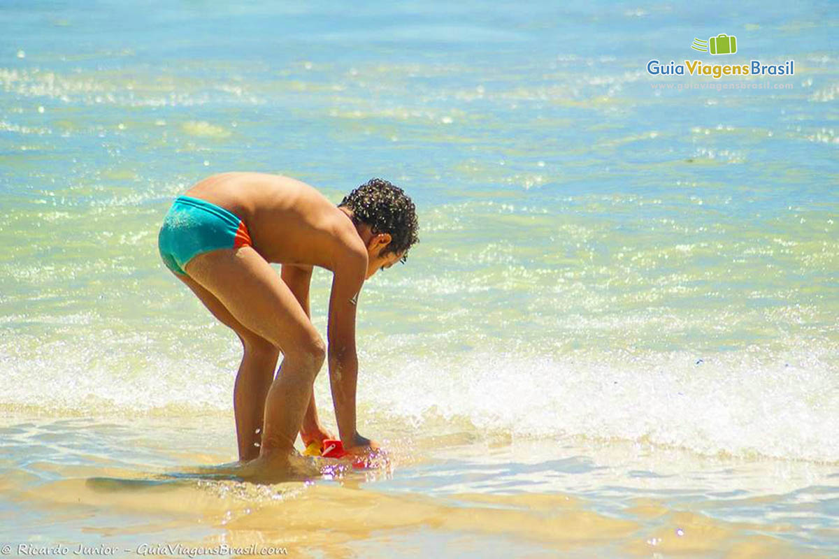Imagem de um menino enchendo o balde com água do mar.