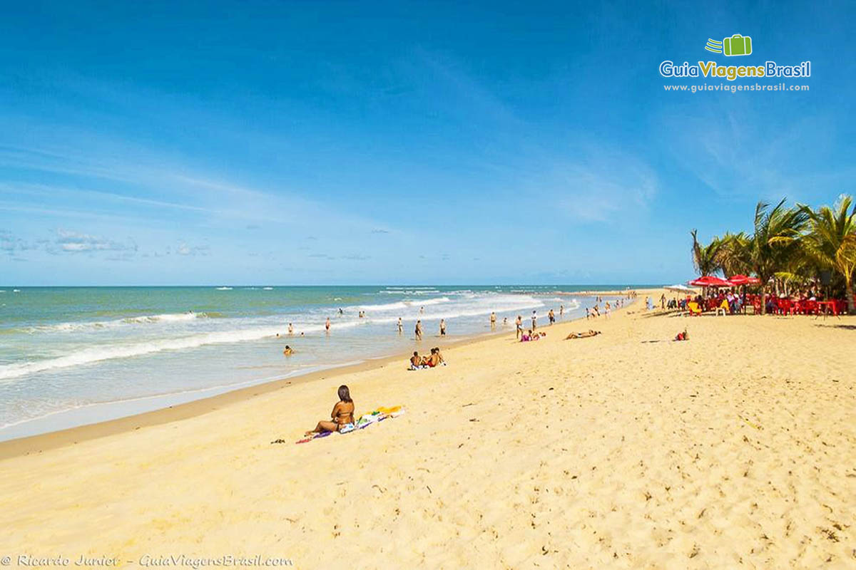 Imagem de vários turistas nas areias e no mar da Praia Nativos.