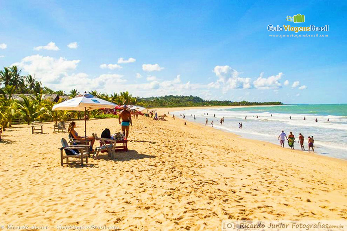 Imagem de turistas em baixo do guarda sol e outros curtindo no mar maravilhoso.