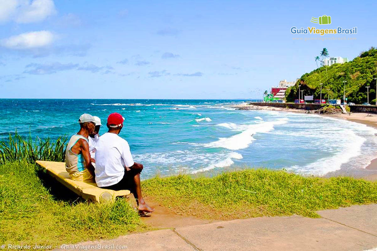 Imagem de amigos sentados no banco conversando e admirando as belezas da Praia Ondina.