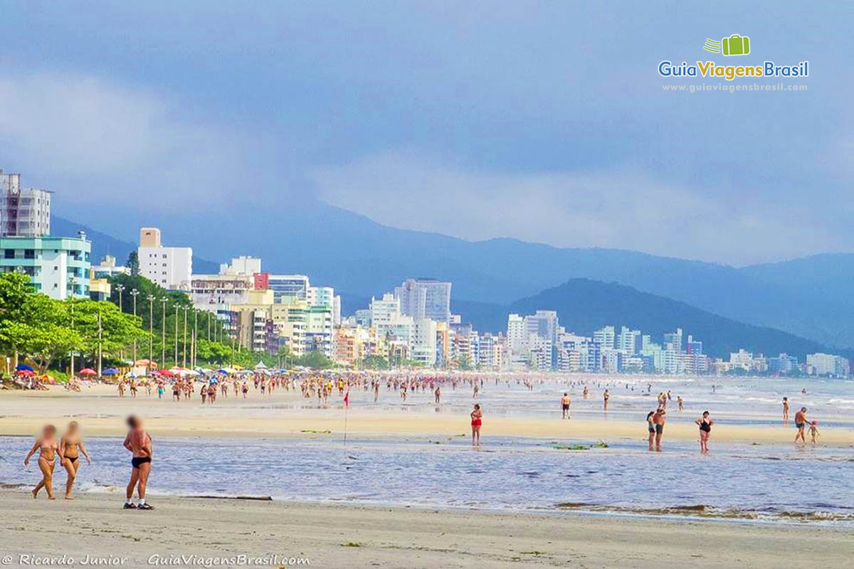 Imagem da praia repleta de banhistas e ao fundo os belos prédios da orla.