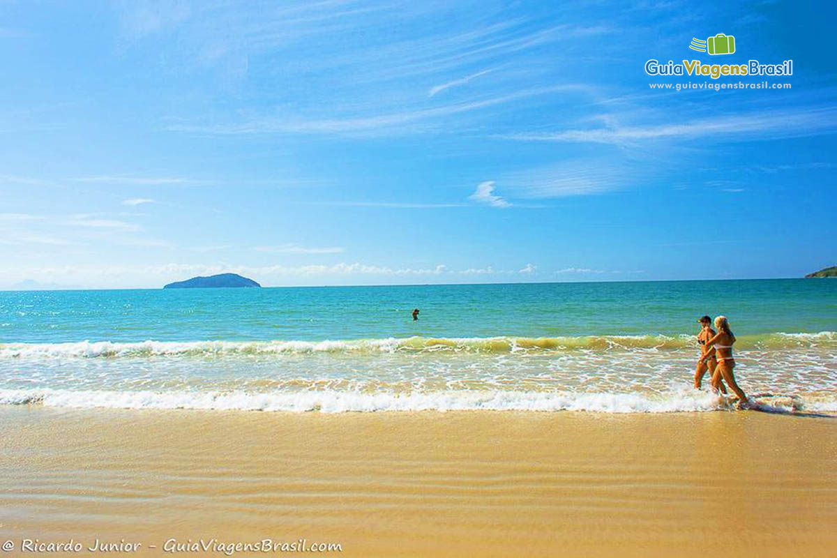 Imagem de amigas caminhando com os pé nas águas da Praia Rasa.