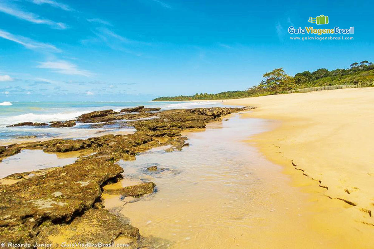 Imagem das águas em volta das pedras na linda praia.