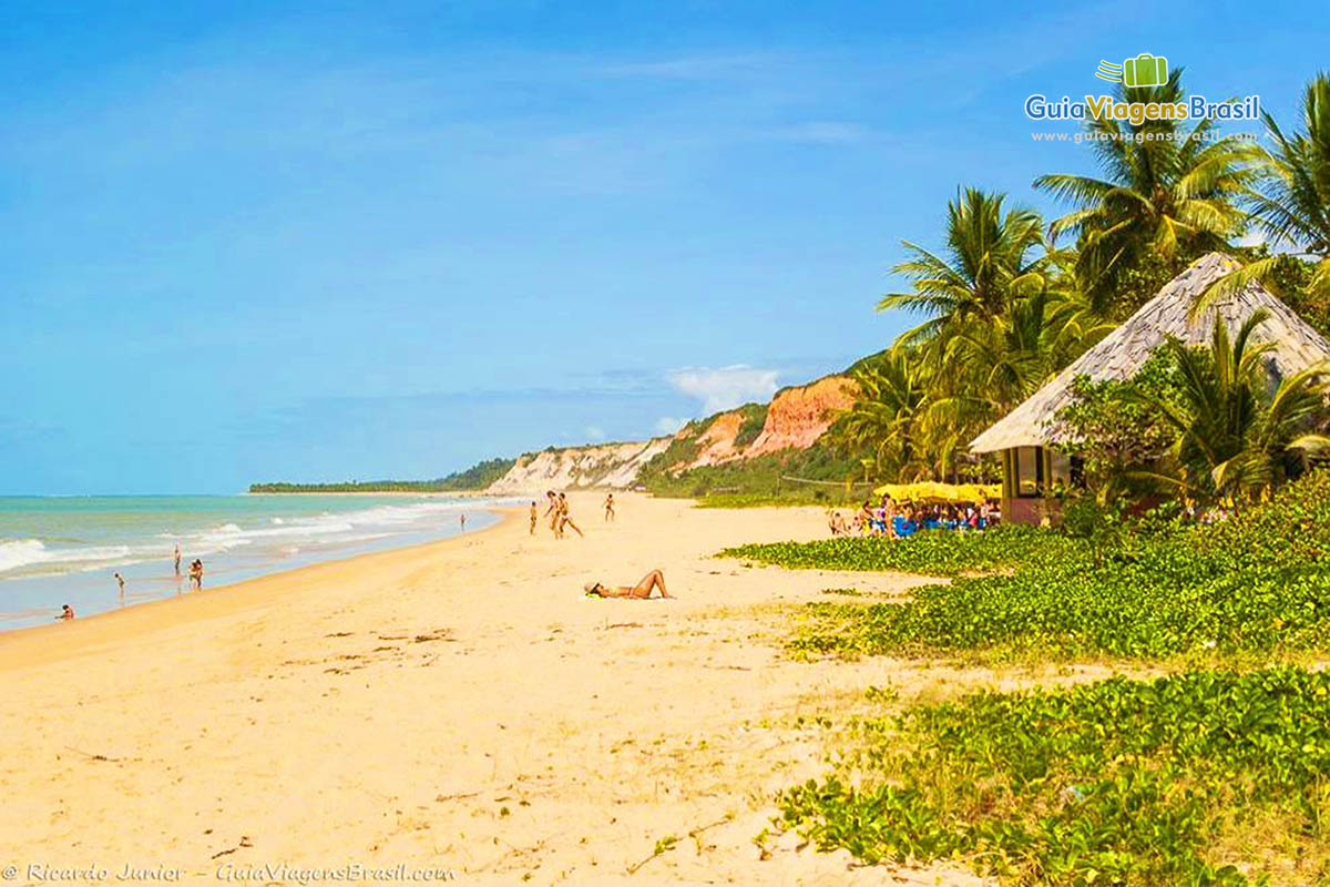 Imagem de quiosque na orla da Praia Taipe e turistas nas areias.