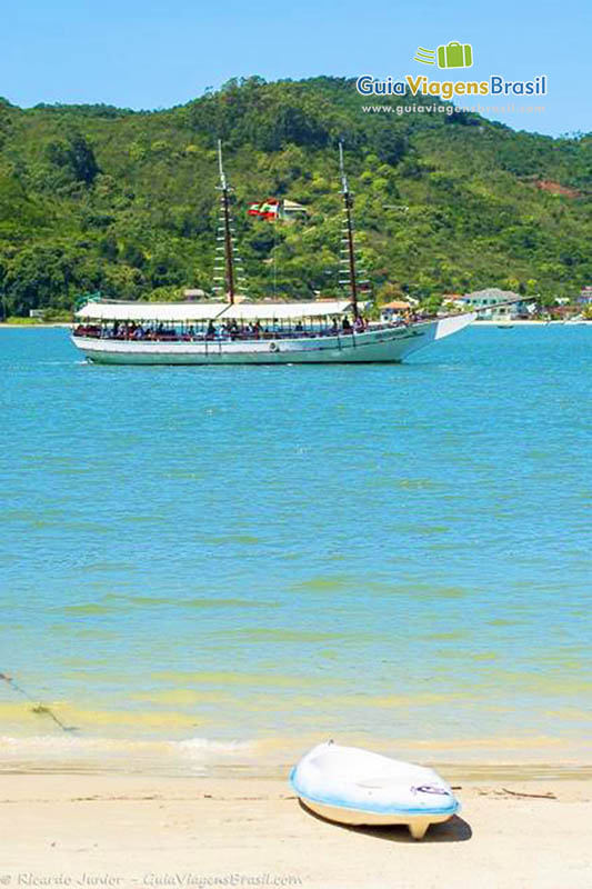 Imagem de uma prancha na beira do mar e ao fundo belo barco de passeio.