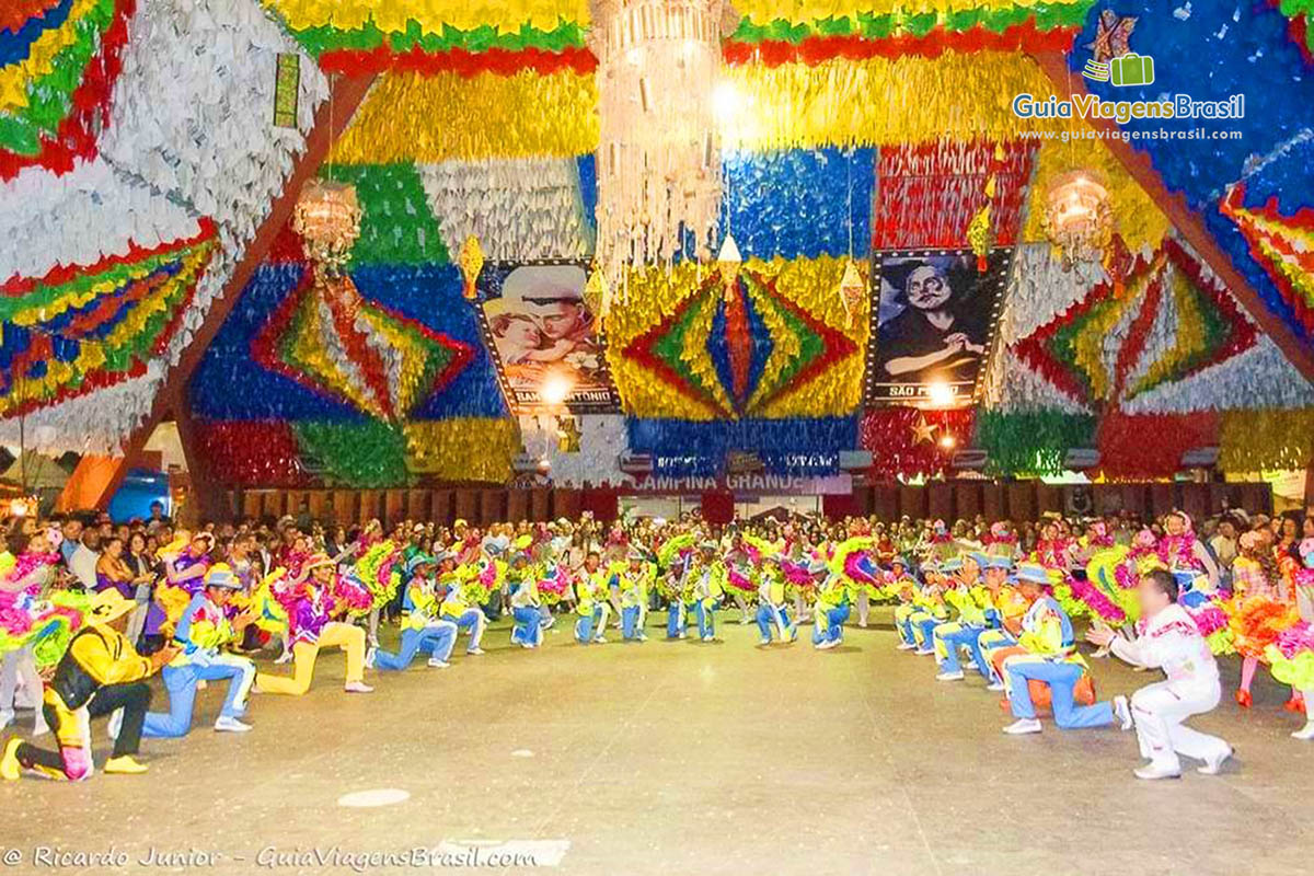 Imagem da quadrilha no meio do salão a o teto do galpão todo enfeitado.