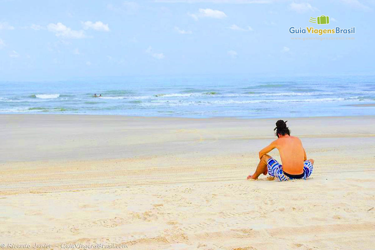 Imagem de um rapaz sentado nas areias admirando as águas do belo Circuito Cabure.