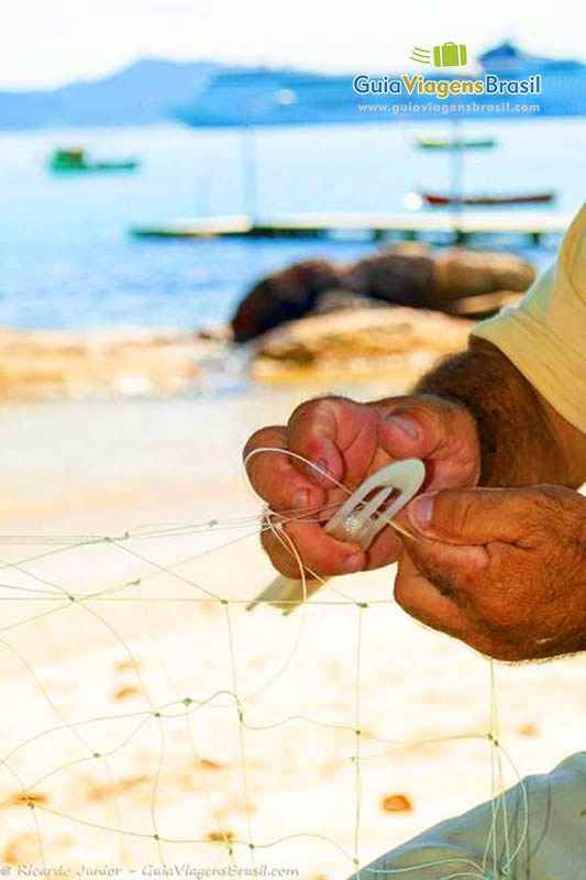 Imagem de pescador costurando rede de pescar.