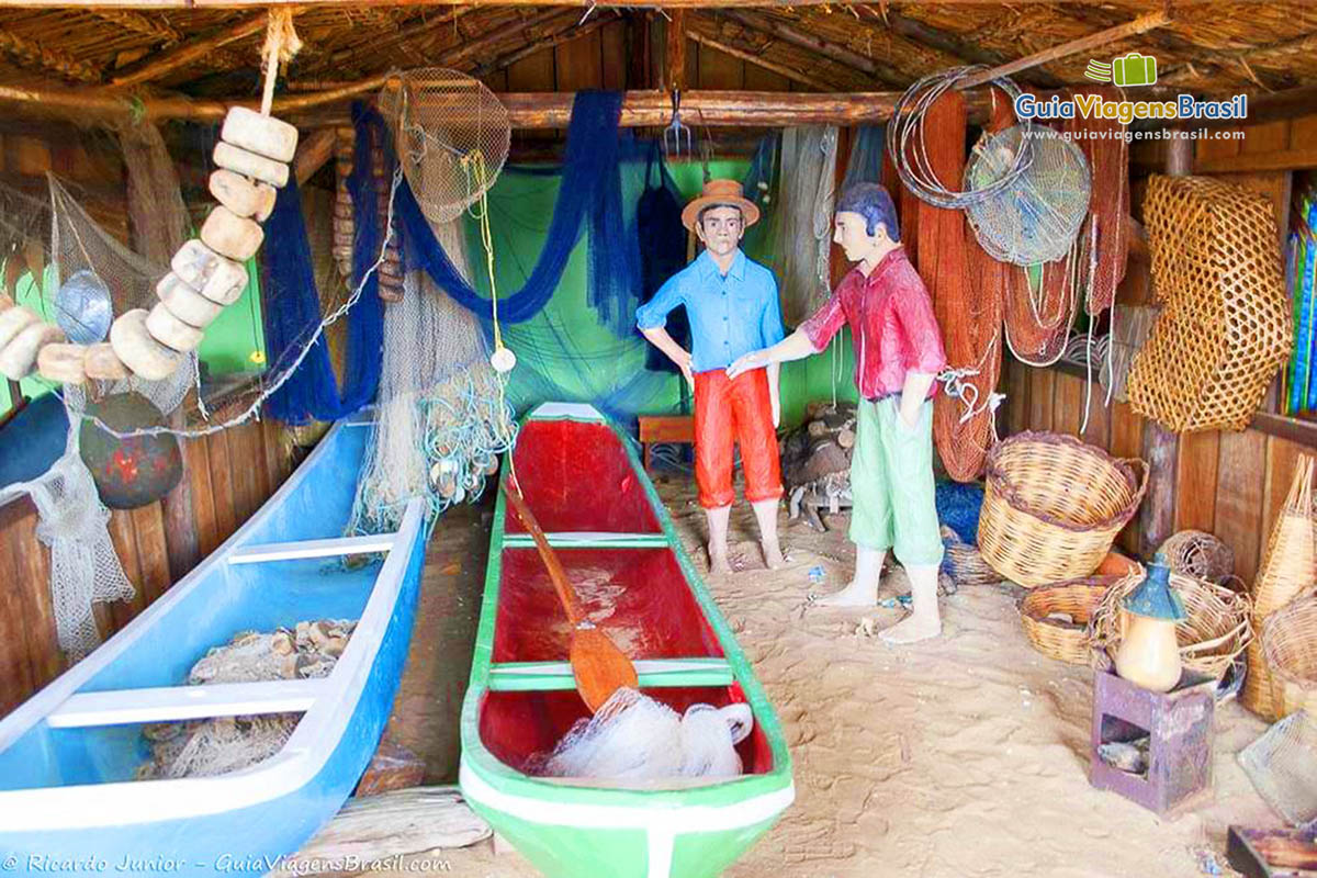Imagem de réplica de barco, pescadores e utensílios de pescar.