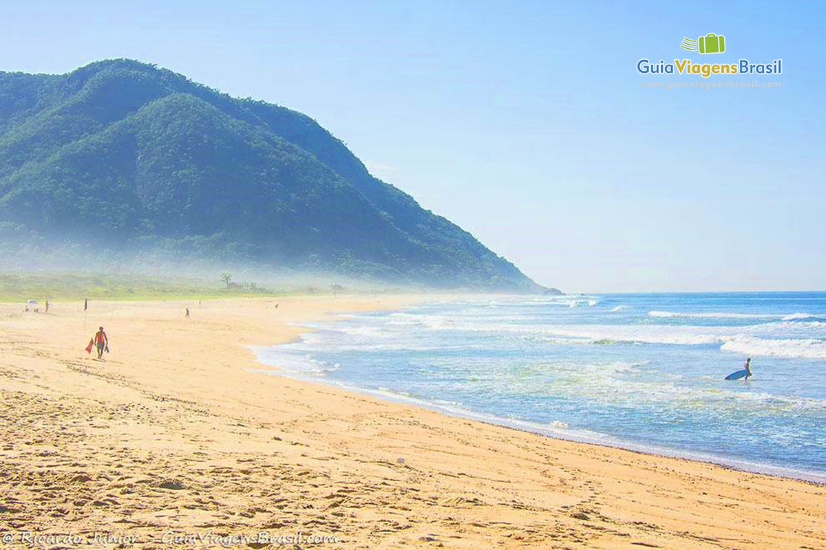 Imagem de salva vidas na areia e surfista entrando no mar da Praia Grumari.