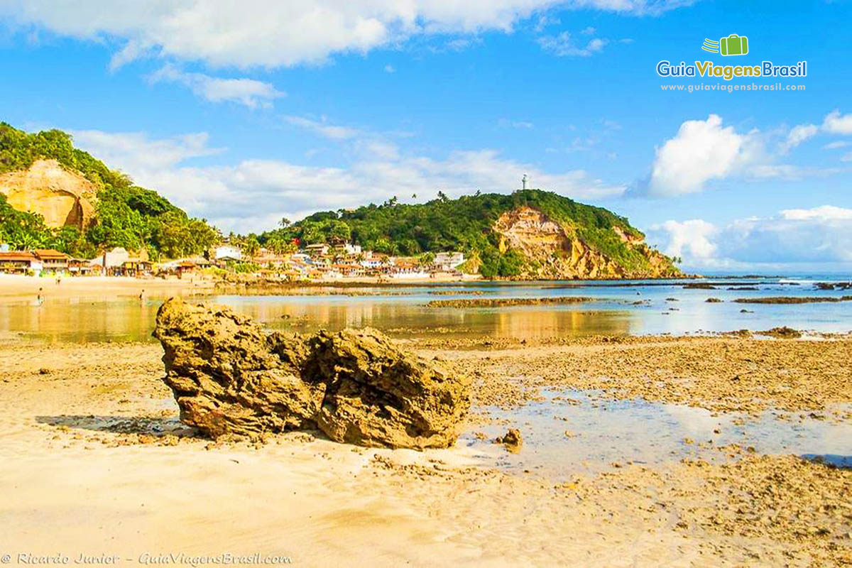 Imagem de pequenas pedras na areia e ao fundo casas no canto na Segunda Praia.