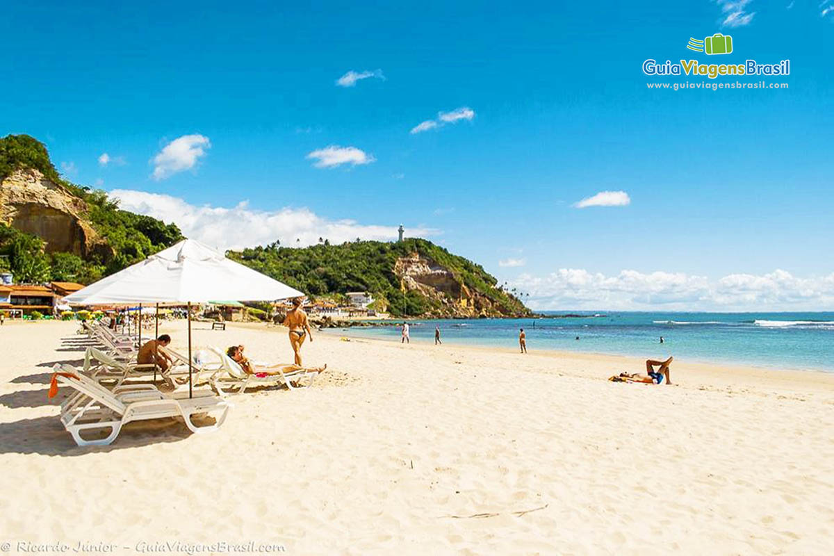 Imagem de turistas nas areias da praia com grandes guarda sol.