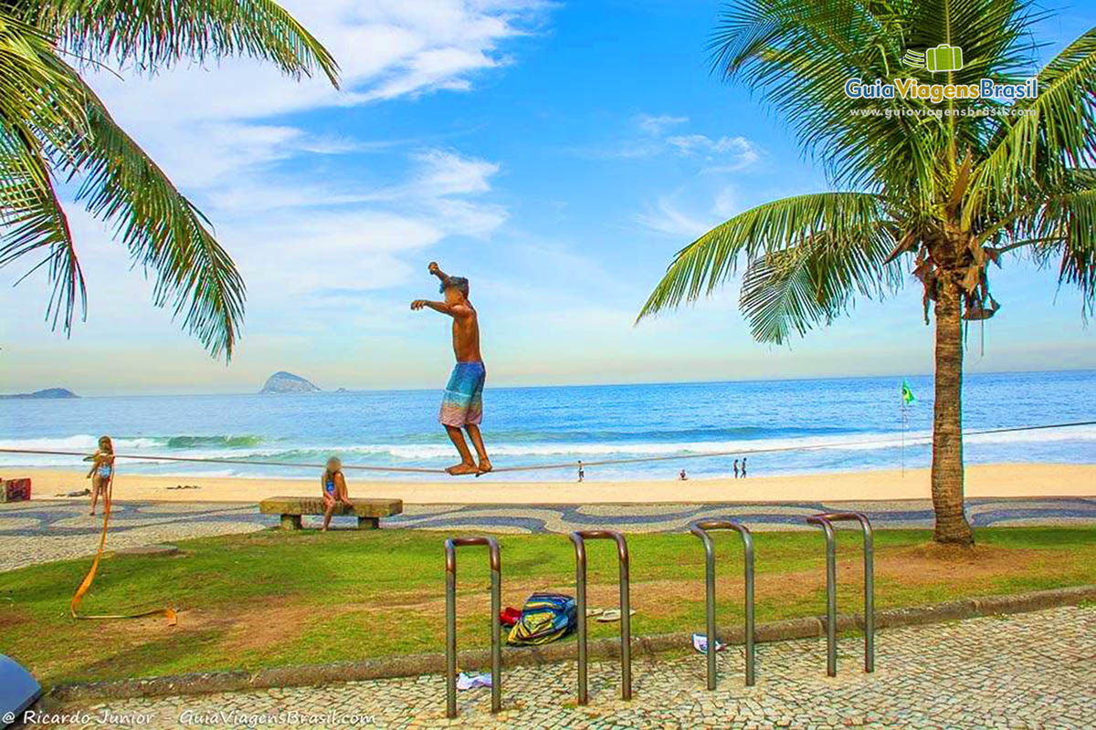 Imagem de um menino praticando slackline na praia.