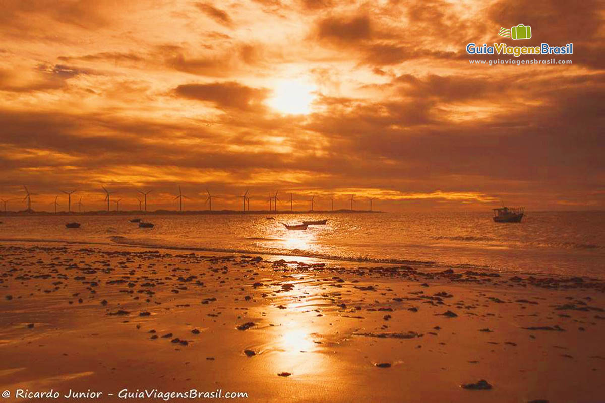 Imagem do sol alaranjado se pondo e refletindo nas águas do mar.