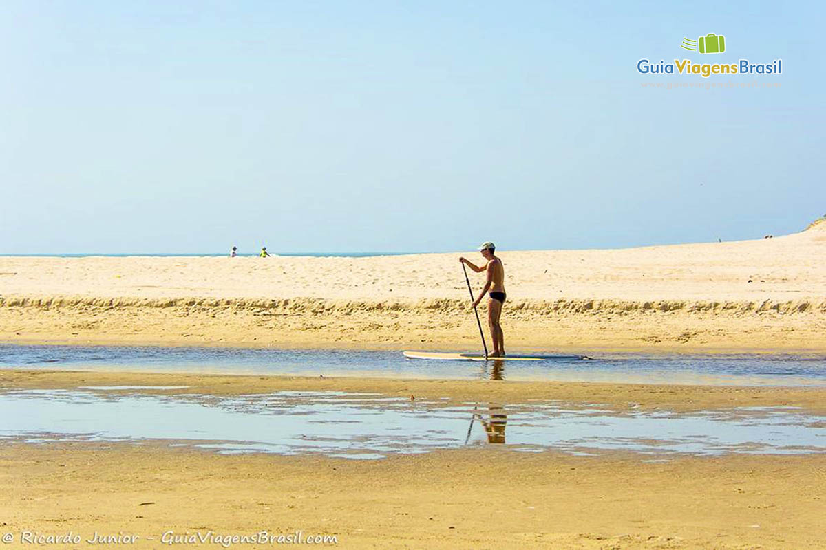 Imagem de uma pessoa praticando stand up paddle na lagoa.