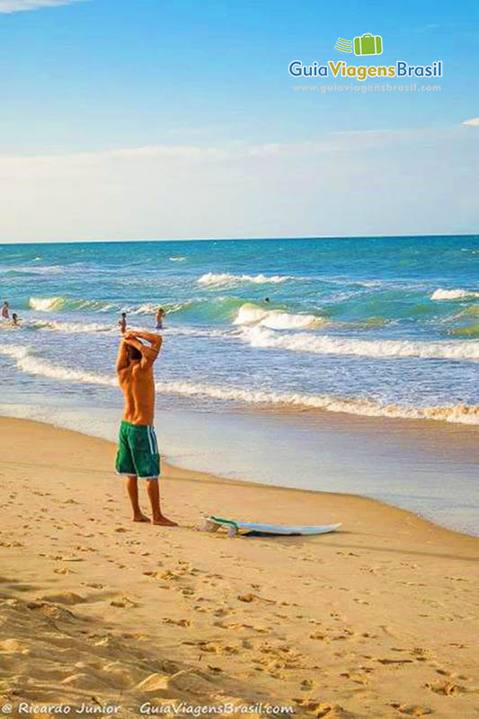 Imagem de surfista se alongando antes de entrar no mar.