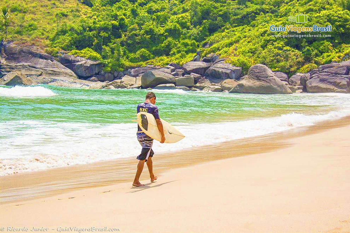 Imagem de um surfista andando nas areias da praia, depois de um dia de belas ondas.