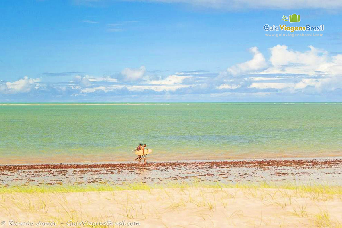 Imagem de surfista andando nas areias da praia.